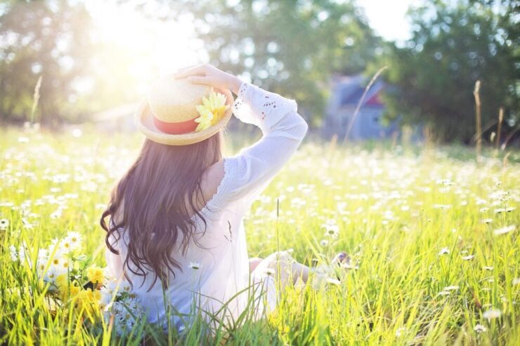 ひとり草むらで、太陽の光を浴びている麦わら帽子の女の子